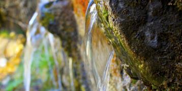 Two small jets of water emerge from a small fountain in a sparsely populated town in Spain