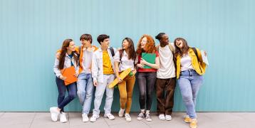 I see a group of happy young people gathered side by side, carrying school bags and exercise books