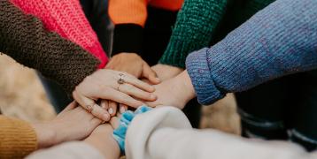 People in colourful sweaters are holding hands as a gesture of collaboration and support. 